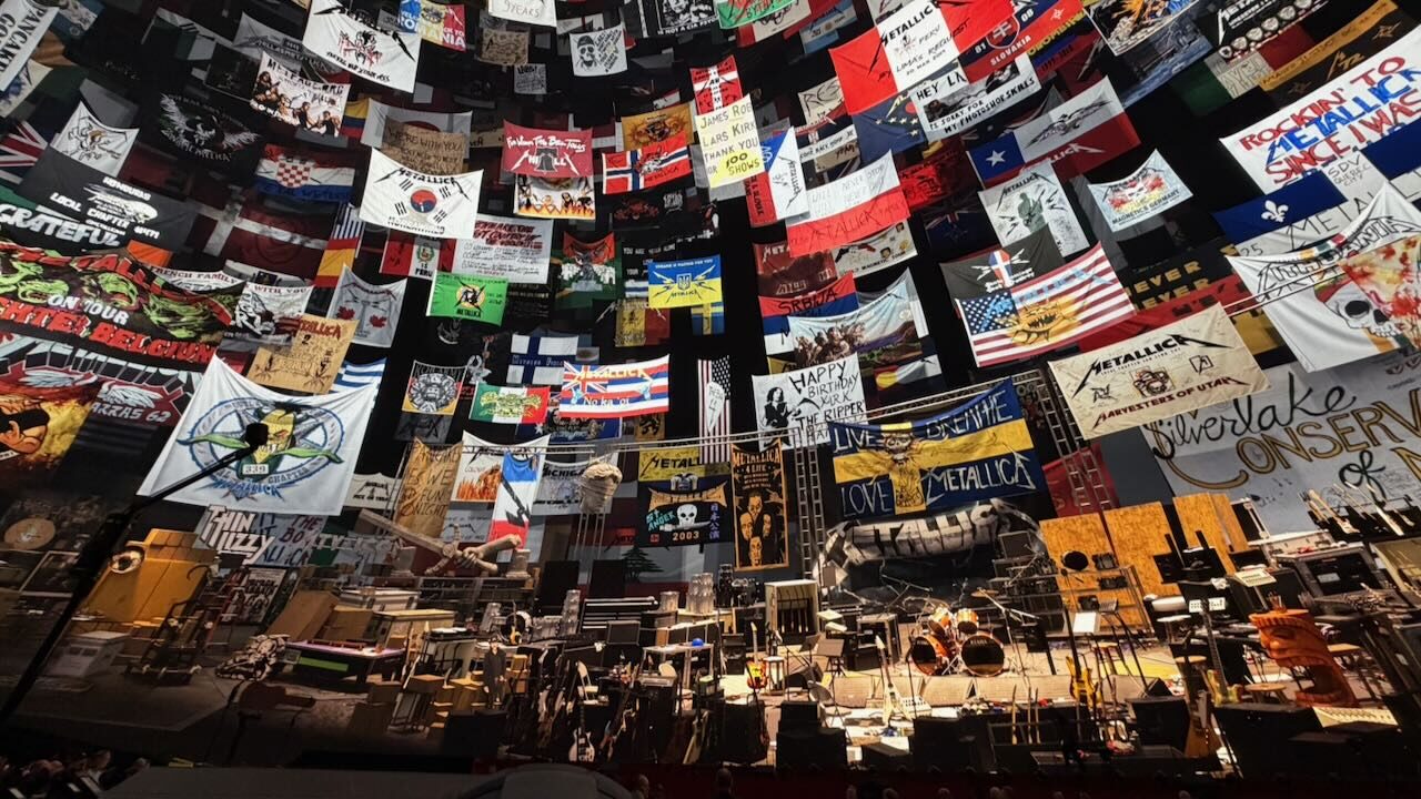 Wide view of the stage inside the Sphere before the show, with the screen above covered in fan club flags