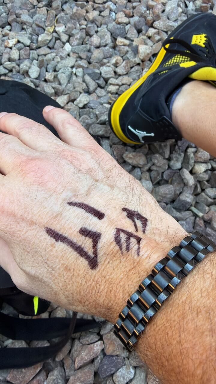 Wesley's hand with a place-in-line number written in Sharpie, above yellow and black Jordans on gravel
