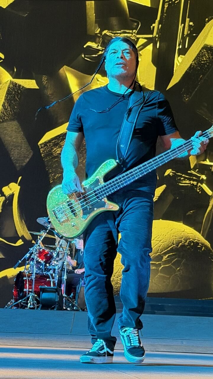 Robert Trujillo playing a teal bass in front of a yellow screen